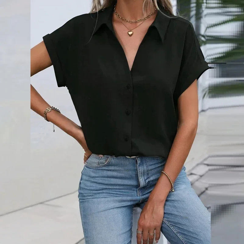 Woman wearing black short-sleeve button-up shirt with gold necklace and blue jeans