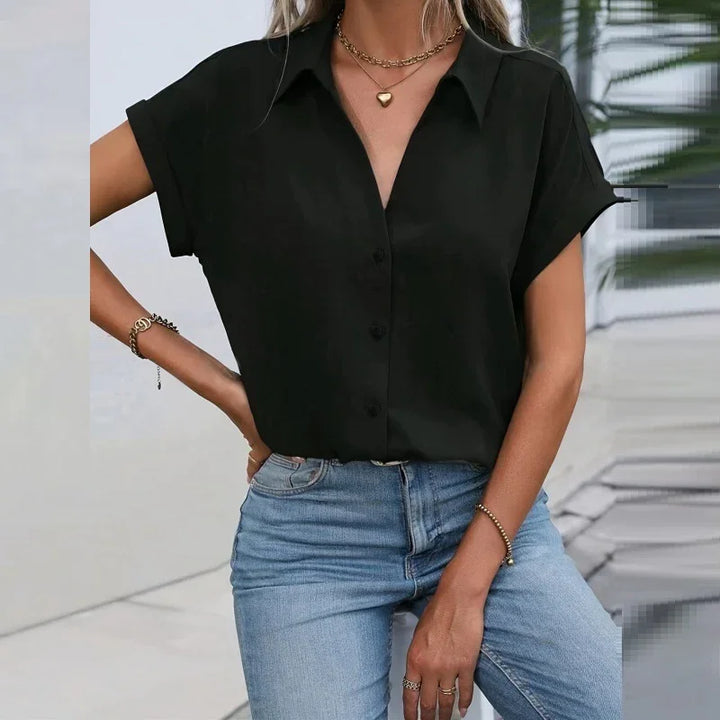 Woman wearing black short-sleeve button-up shirt with gold necklace and blue jeans