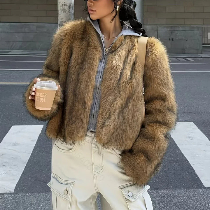 Woman in brown faux fur jacket, grey hoodie, beige cargo pants holding coffee cup on city street