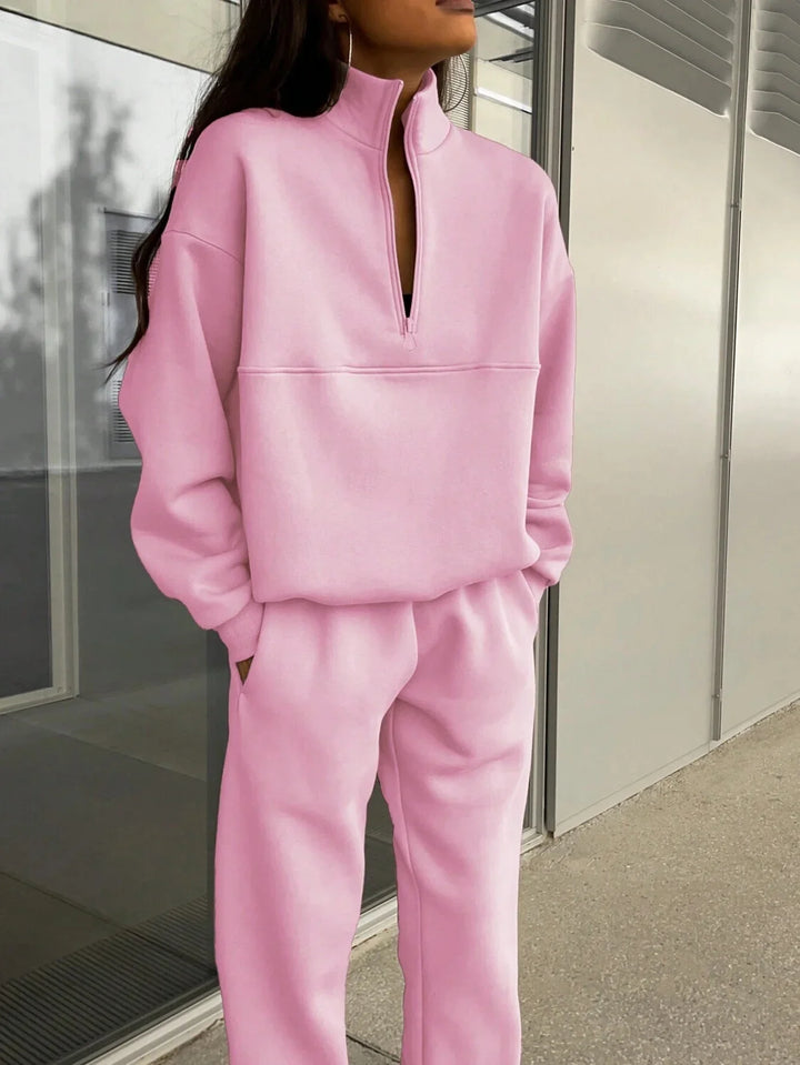 Woman wearing a pink zip-up sweatshirt and matching sweatpants with hands in pockets