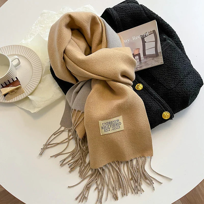 Beige and gray fringed scarf with Undreson Registered EST. 2023 label on black textured coat with gold buttons on a white table