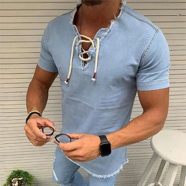 Man wearing light blue distressed short sleeve denim shirt with lace-up neckline holding sunglasses