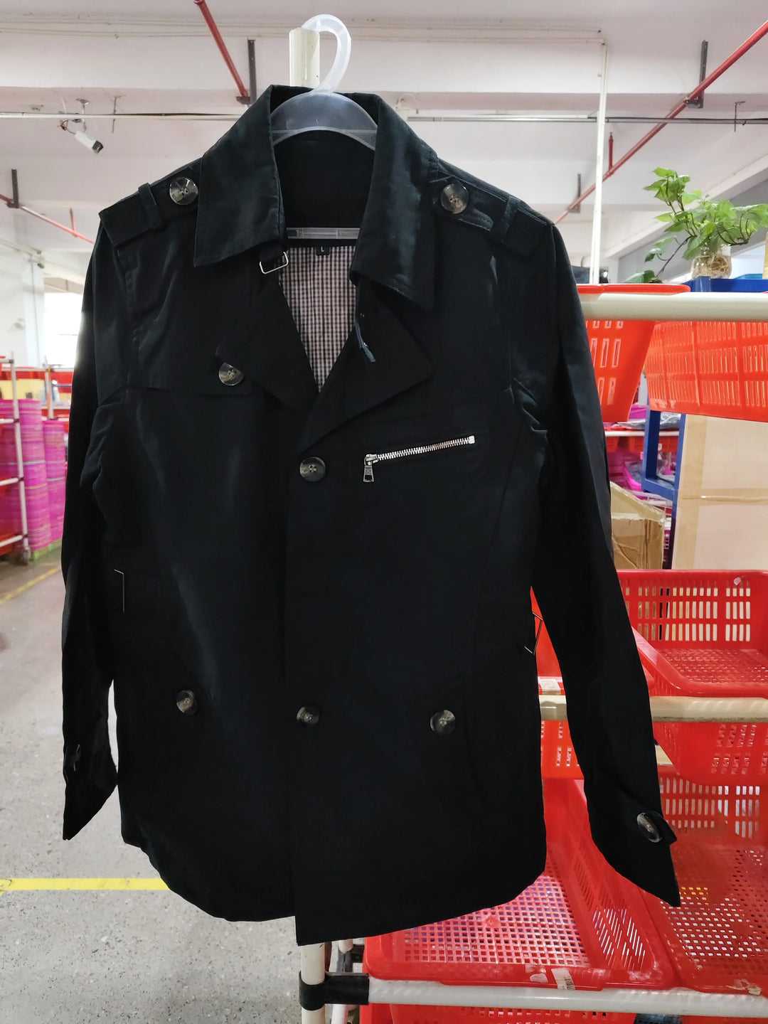 Black double-breasted jacket with buttons and zip pocket on hanger in warehouse setting