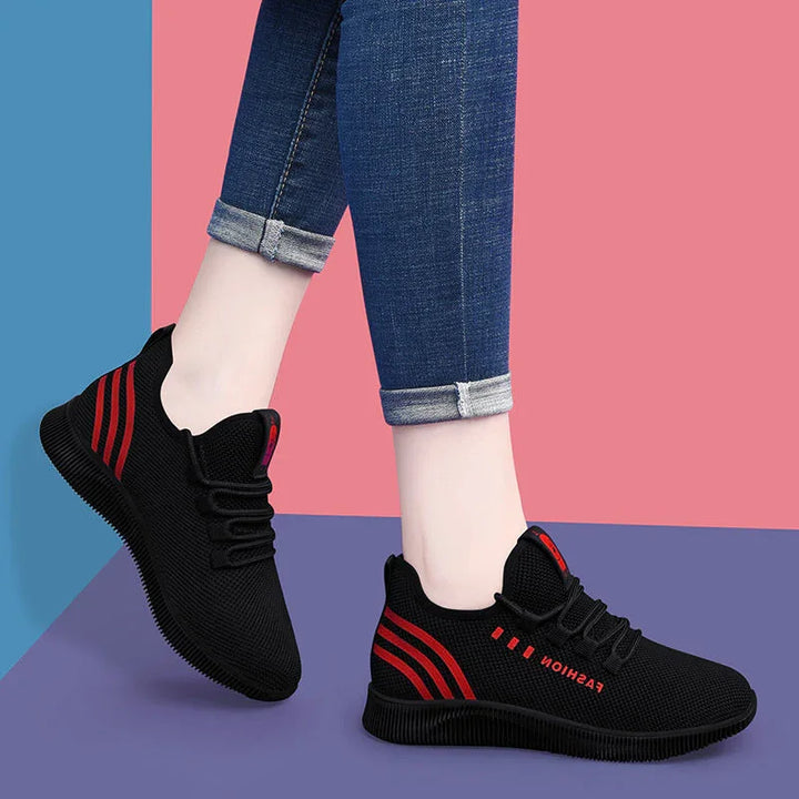 Black mesh sneakers with red stripes and "FASHION" text, worn with rolled-up blue jeans on colorful background