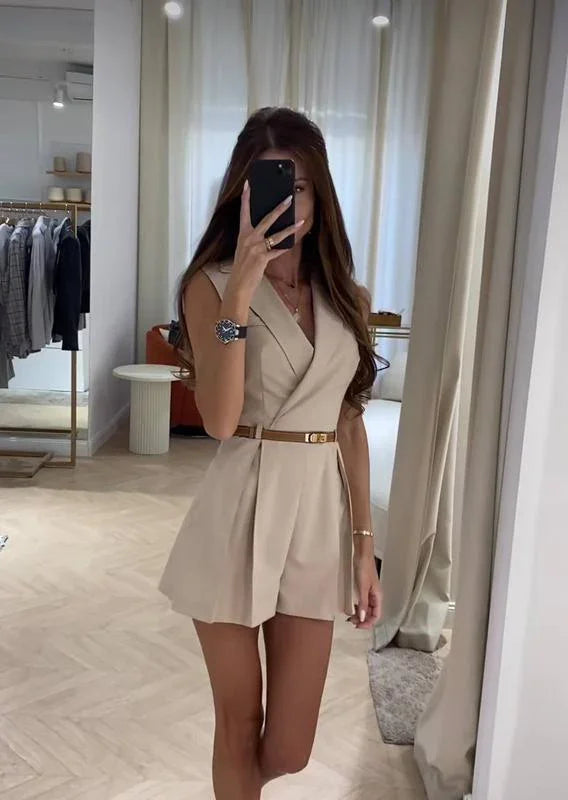 woman taking mirror selfie wearing beige sleeveless belted romper in stylish boutique