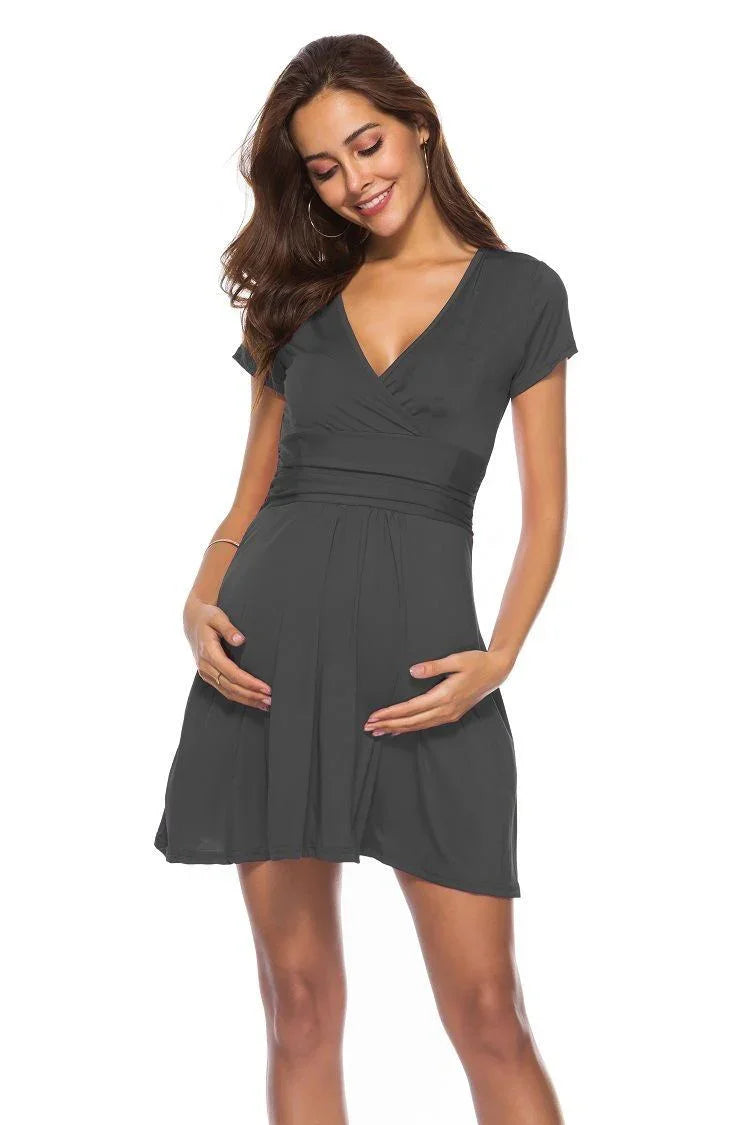 Smiling pregnant woman wearing a short black maternity dress with a v-neck and cap sleeves