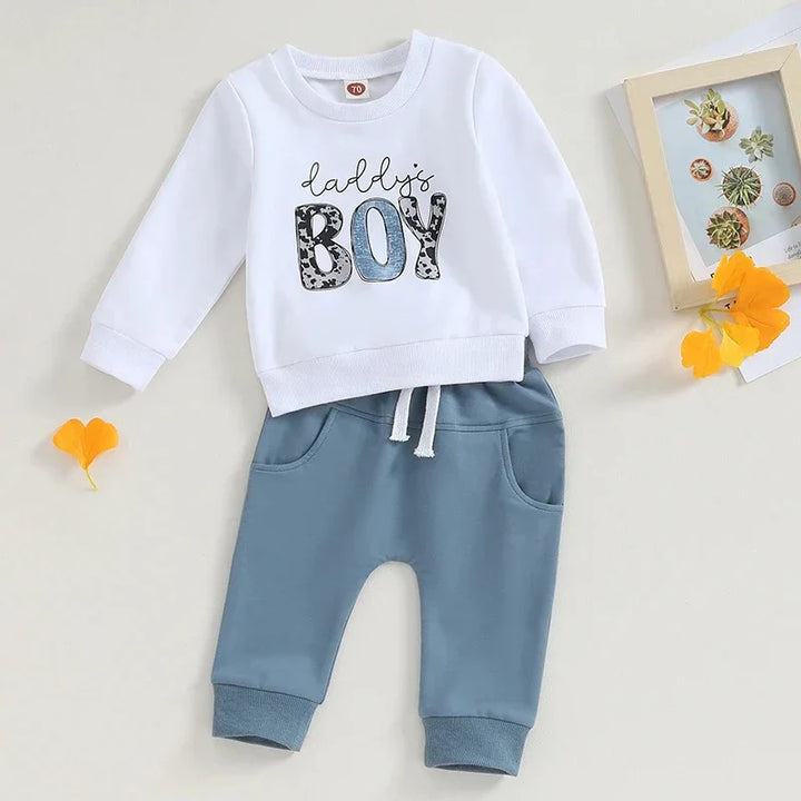 White long-sleeve baby shirt with 'Daddy's Boy' text and blue pants with drawstring on light background