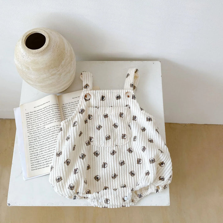 Cream baby romper with black polka dot pattern on white table beside an open book and ceramic vase