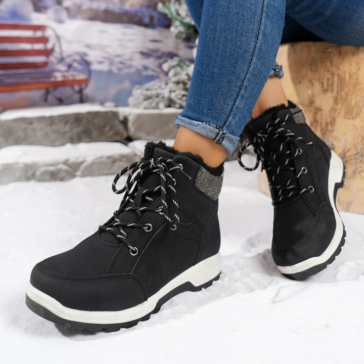 Black winter boots with fur lining and white soles worn with blue jeans on snowy ground