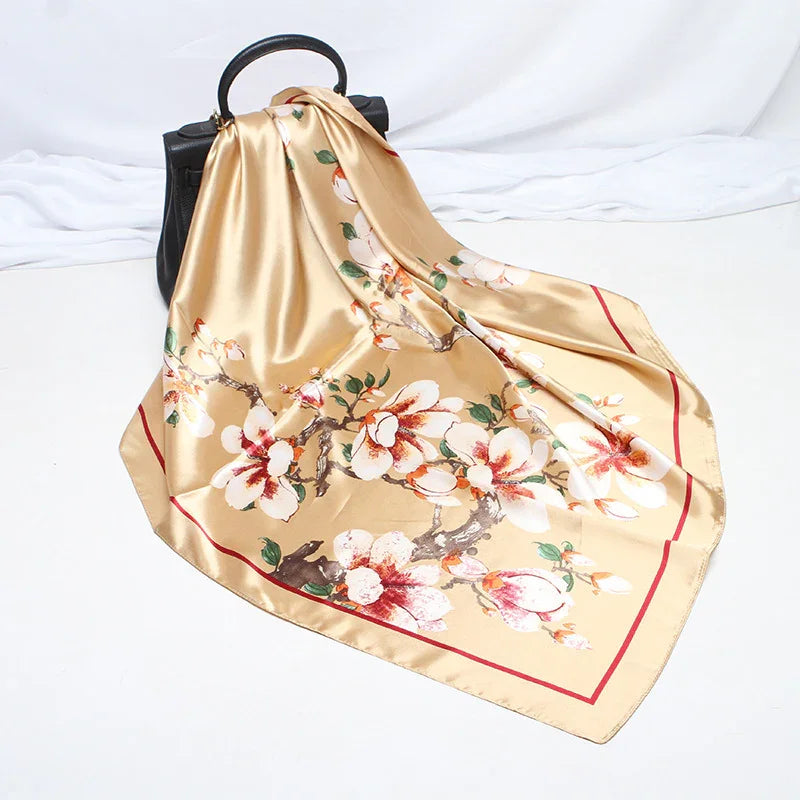 Beige satin scarf with floral print draped over black handbag on white background