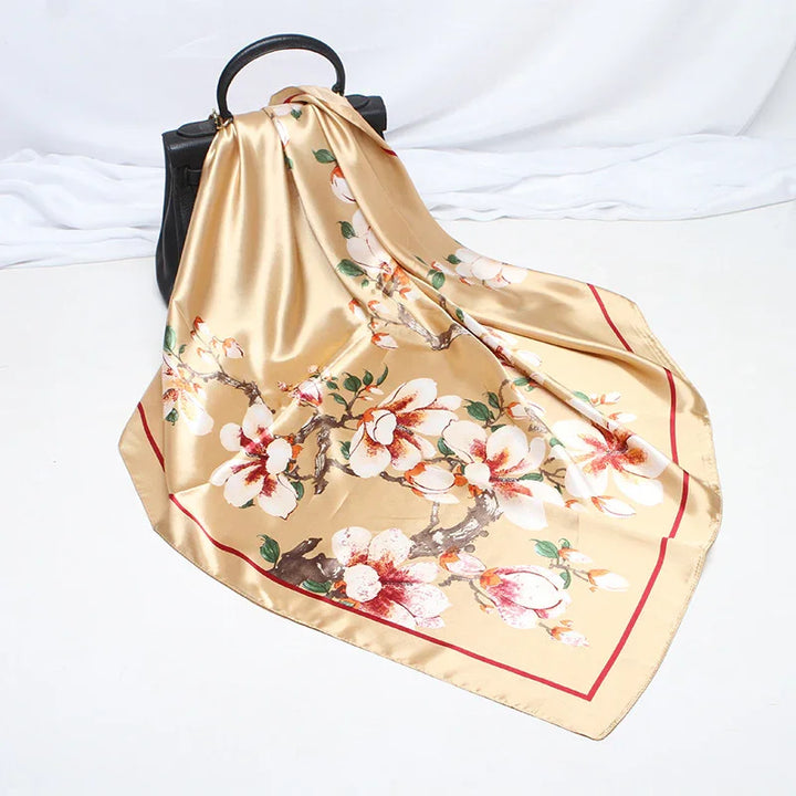 Beige satin scarf with floral print draped over black handbag on white background