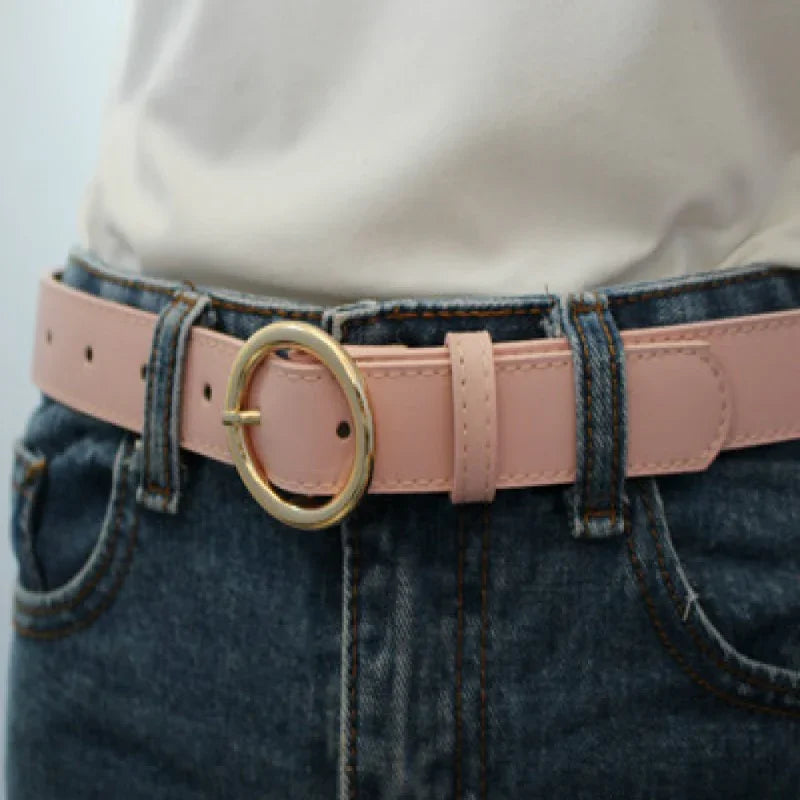 Close-up of pink leather belt with gold oval buckle worn with blue denim jeans and white shirt