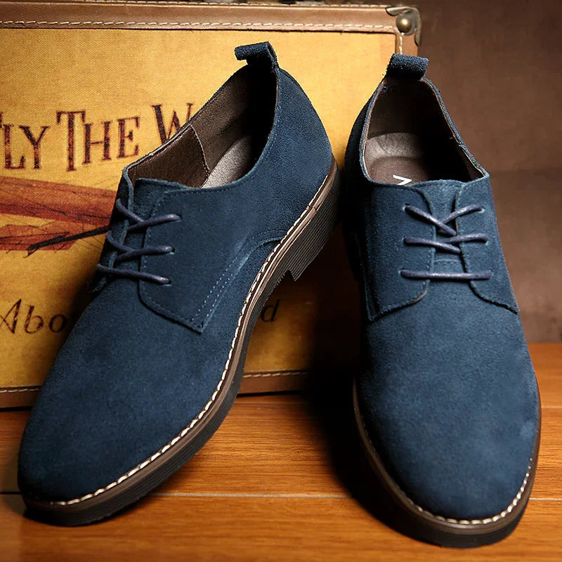 Pair of navy blue suede casual men's shoes with brown soles on wooden floor