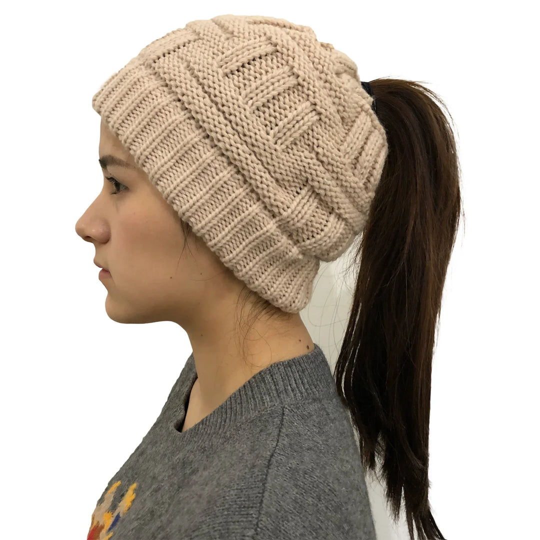 Profile of woman wearing beige knitted beanie hat with ponytail hole and gray sweater