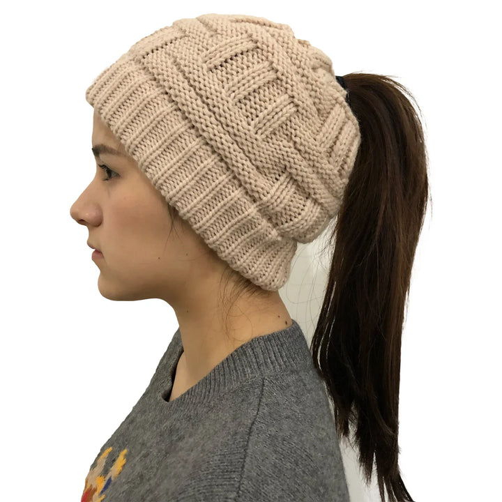 Profile of woman wearing beige knitted beanie hat with ponytail hole and gray sweater