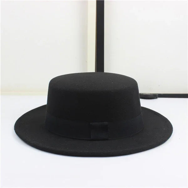 Black flat-brimmed fedora hat with a ribbon band on a white surface