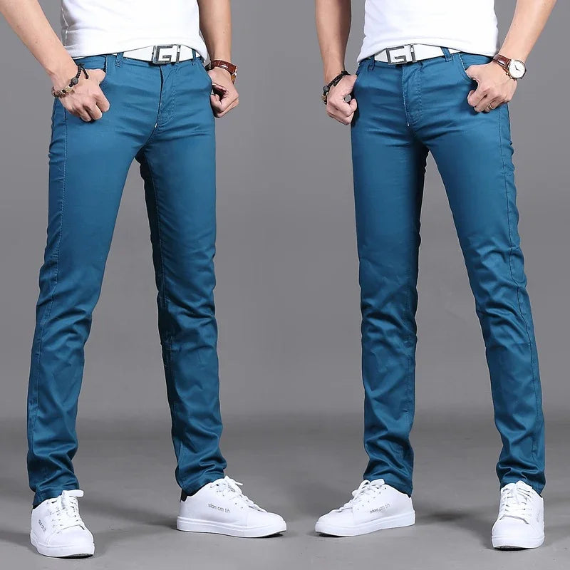 Man wearing slim fit blue pants, white sneakers, white belt, and accessories against gray background