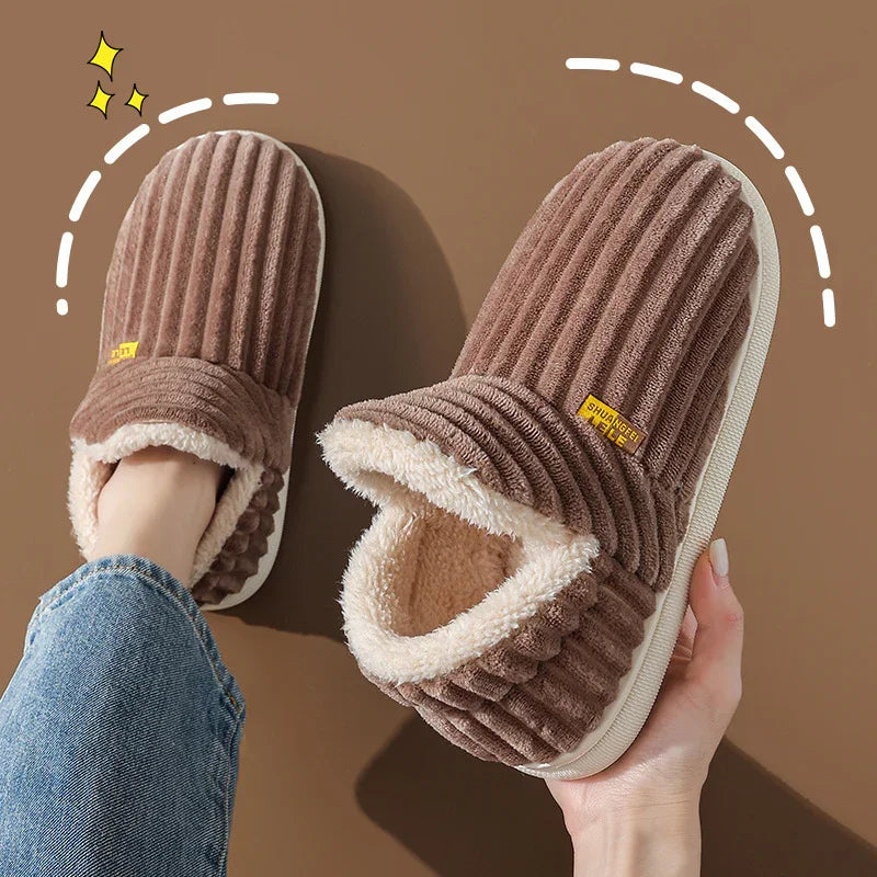 Brown ribbed plush indoor slippers with white fleece lining, worn by a person in jeans
