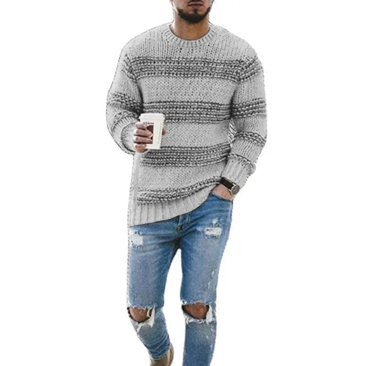 Man wearing gray striped knit sweater and ripped blue jeans holding coffee cup