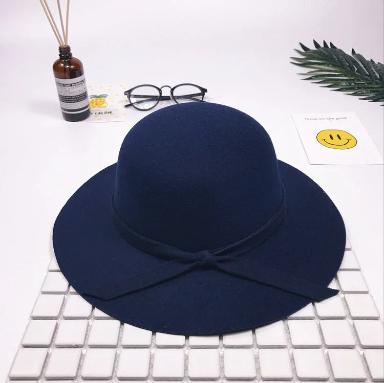 Navy blue wide-brimmed felt hat with a bow band, styled with black round glasses and decorative items