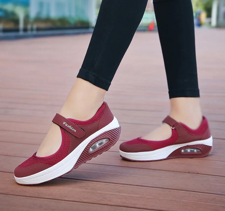 Woman wearing burgundy mesh Mary Jane style sneakers with air cushion sole on wooden deck