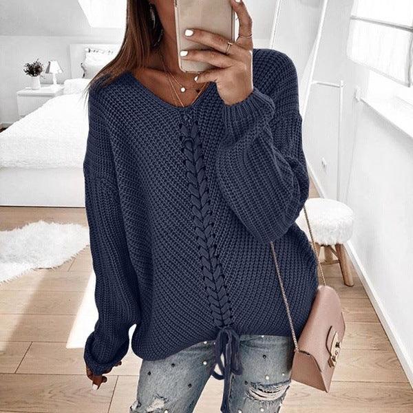Woman wearing navy blue knit sweater with V-neck and tie hem, paired with distressed jeans in bright bedroom