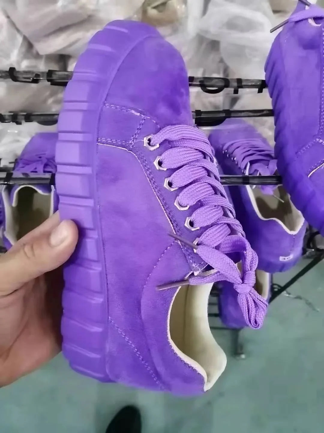 Hand holding purple suede sneaker with thick sole and laces in shoe manufacturing setting