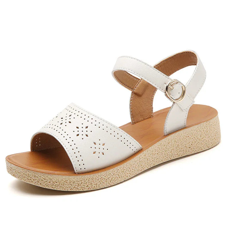 White leather open-toe sandal with perforated floral design, ankle strap, and textured wedge sole