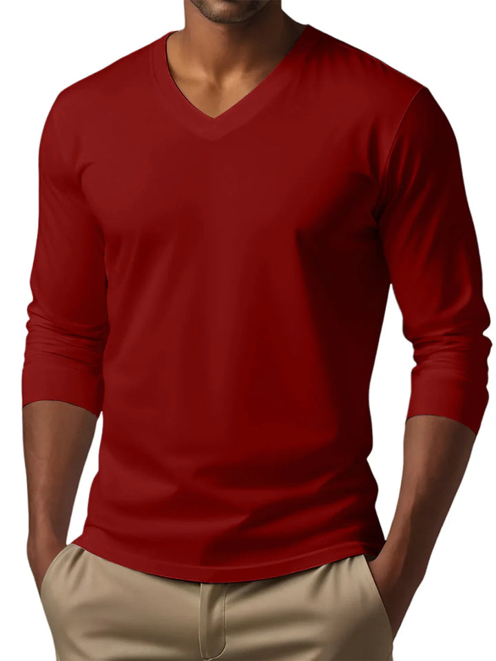 Man wearing a fitted red long-sleeve V-neck shirt with beige pants, hands in pockets