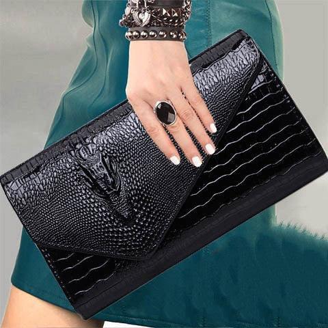Black textured leather clutch purse held by hand with black ring and studded bracelets, model wearing green dress