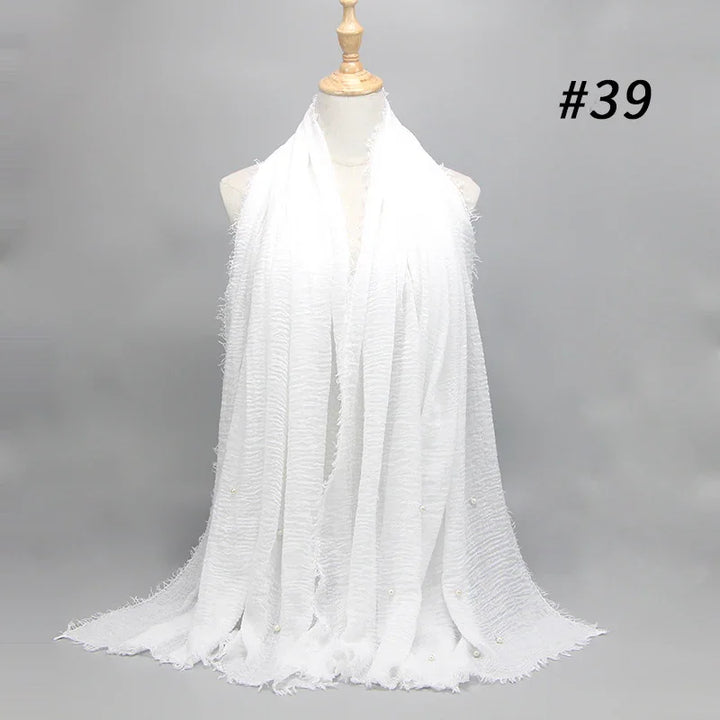 White textured scarf with fringe and small pearl embellishments displayed on mannequin against gray background