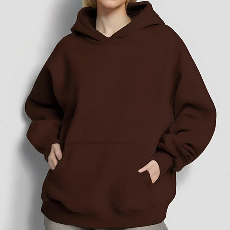 Person wearing a brown oversized hoodie with front pocket and hood, hands in pockets