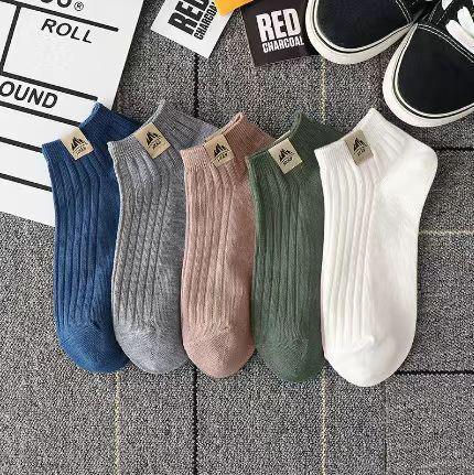 Set of five ribbed ankle socks in blue, gray, pink, green, and white on a gray carpet with black sneakers nearby
