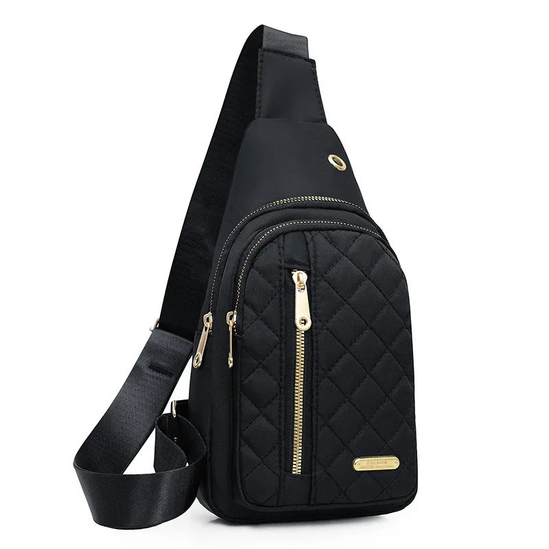 Black quilted sling backpack with gold zippers and adjustable strap on white background