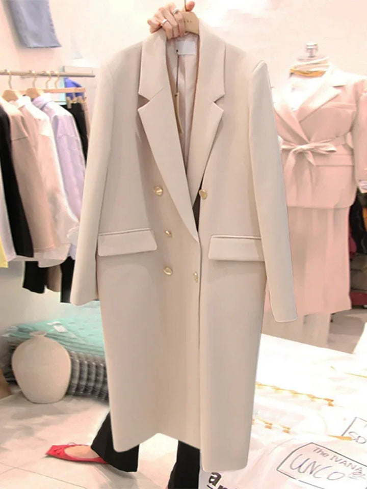 Hand holding beige double-breasted long blazer with gold buttons in a clothing store