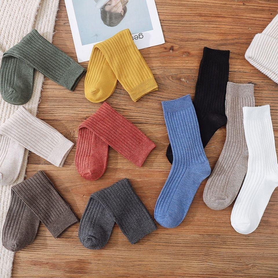 Variety of colorful ribbed knit socks laid out on wooden surface including green, yellow, red, blue, black, white, beige, gray, and brown pairs