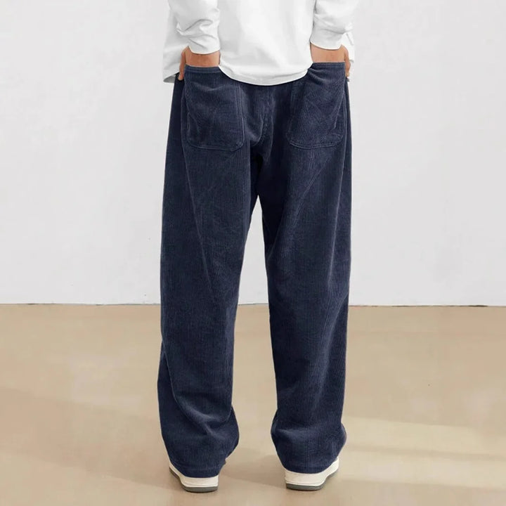 Back view of person wearing loose-fitting navy blue corduroy pants with patch pockets and white sneakers