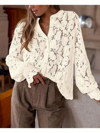 Woman wearing elegant white lace long-sleeve blouse paired with high-waisted brown pants in cozy indoor setting