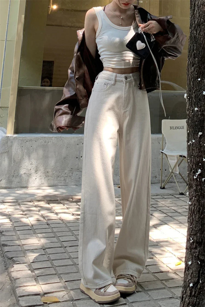 Woman in white tank top, beige wide-leg pants, brown leather jacket outdoors with black purse
