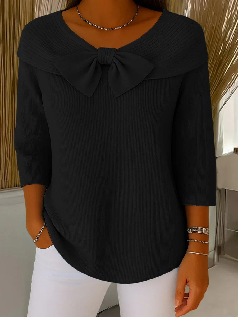 Black ribbed knit top with large bow neckline and 3/4 sleeves paired with white pants