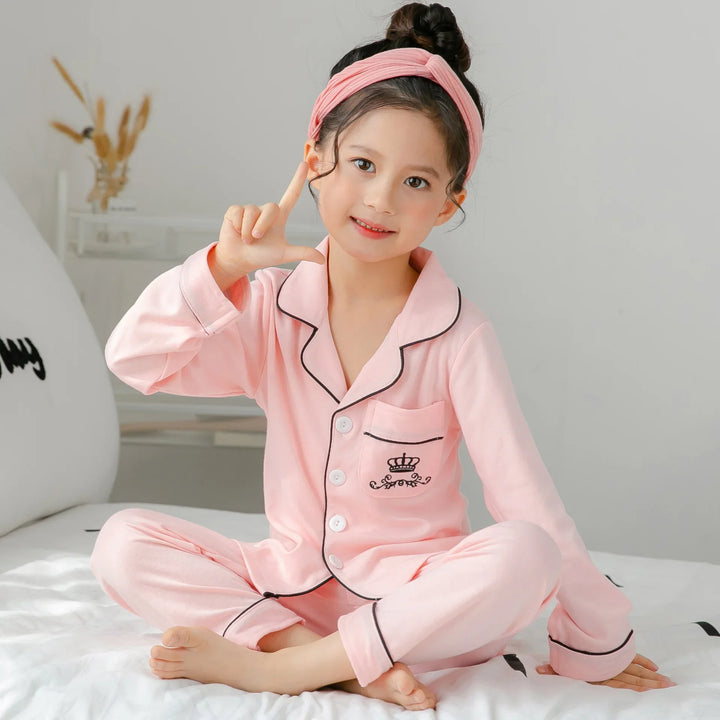 Young girl sitting cross-legged on bed wearing pink pajamas and matching headband in bright room