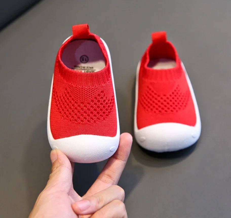 Pair of red baby shoes with white soles on gray background, one held by hand