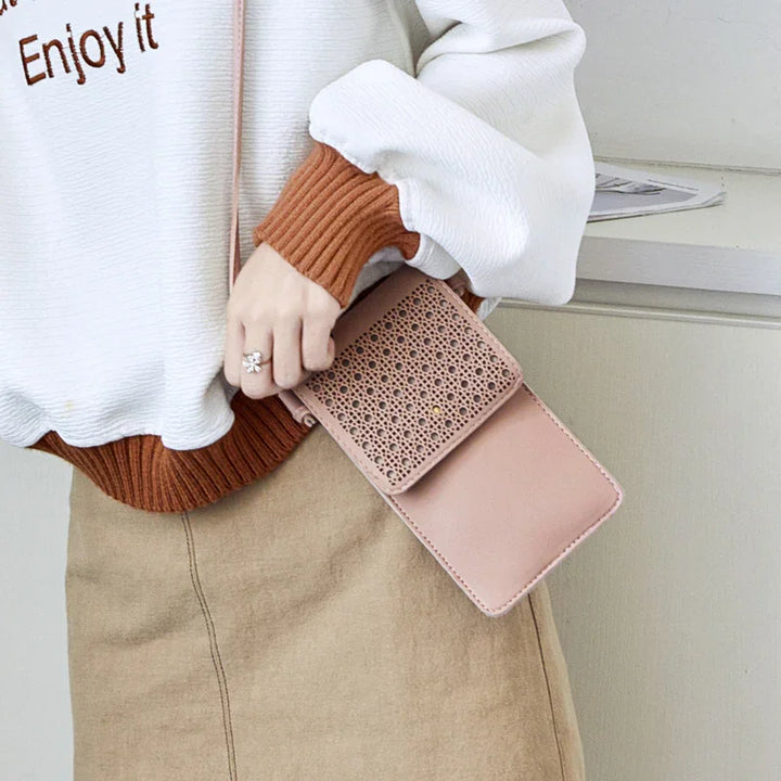 Woman holding a pink woven flap crossbody bag wearing white sweater with brown cuffs and beige skirt