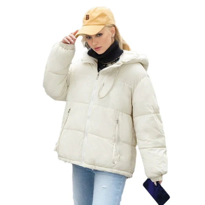 Woman wearing cream puffer jacket with hood, beige cap, black turtleneck, and light blue jeans holding phone