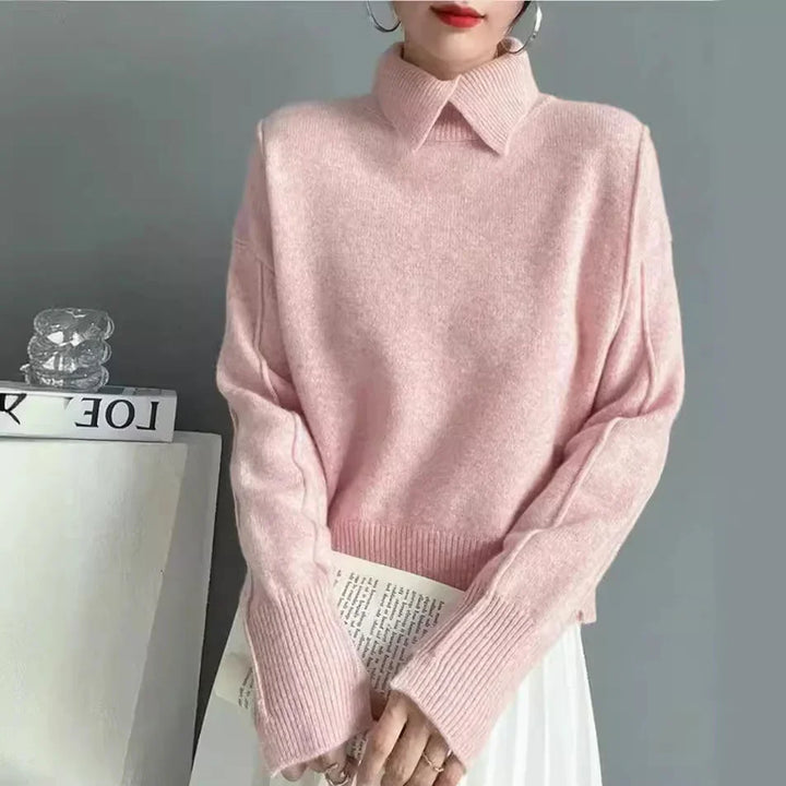 Woman wearing soft pink knit sweater with collar and ribbed cuffs holding book against gray background