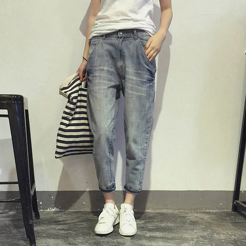 Person wearing faded blue cropped jeans, white sneakers, white t-shirt, holding striped tote bag indoors