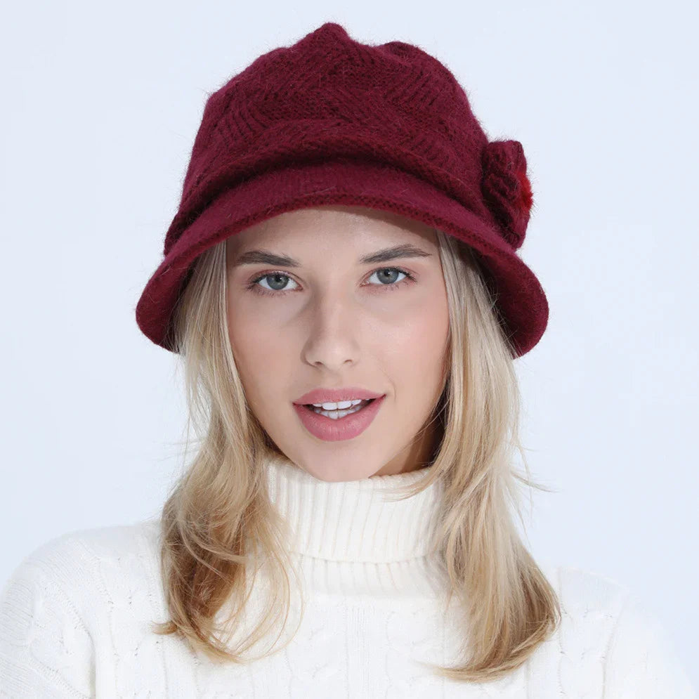 Blonde woman wearing a burgundy knit bucket hat with a flower detail and a white turtleneck sweater