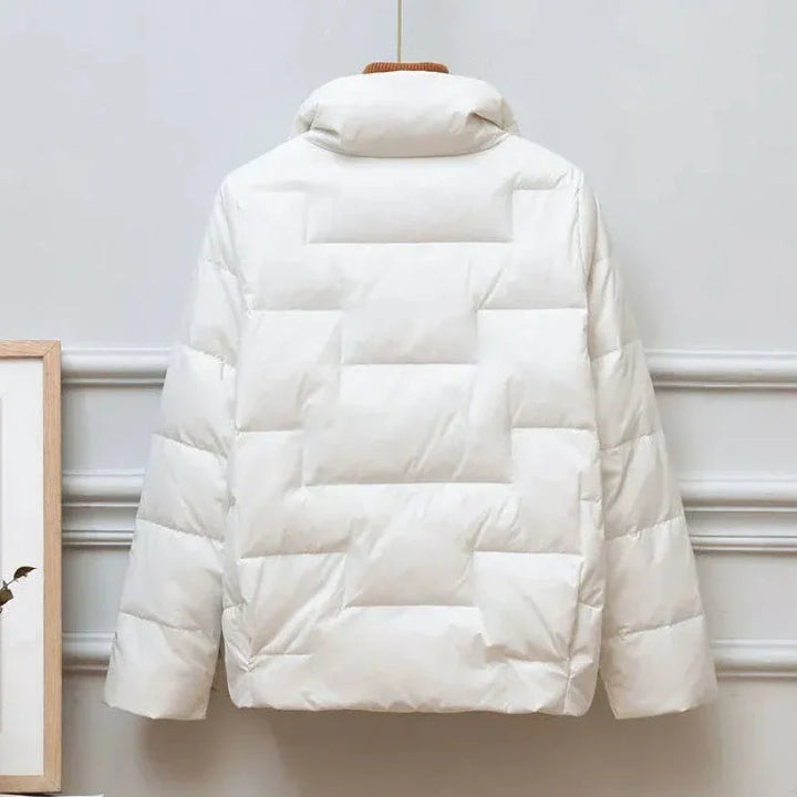 Back view of a white quilted puffer jacket with high collar hanging indoors