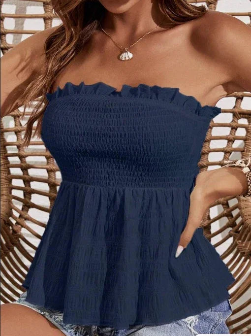 Woman wearing navy blue strapless smocked top with ruffle edge, seated on wicker chair