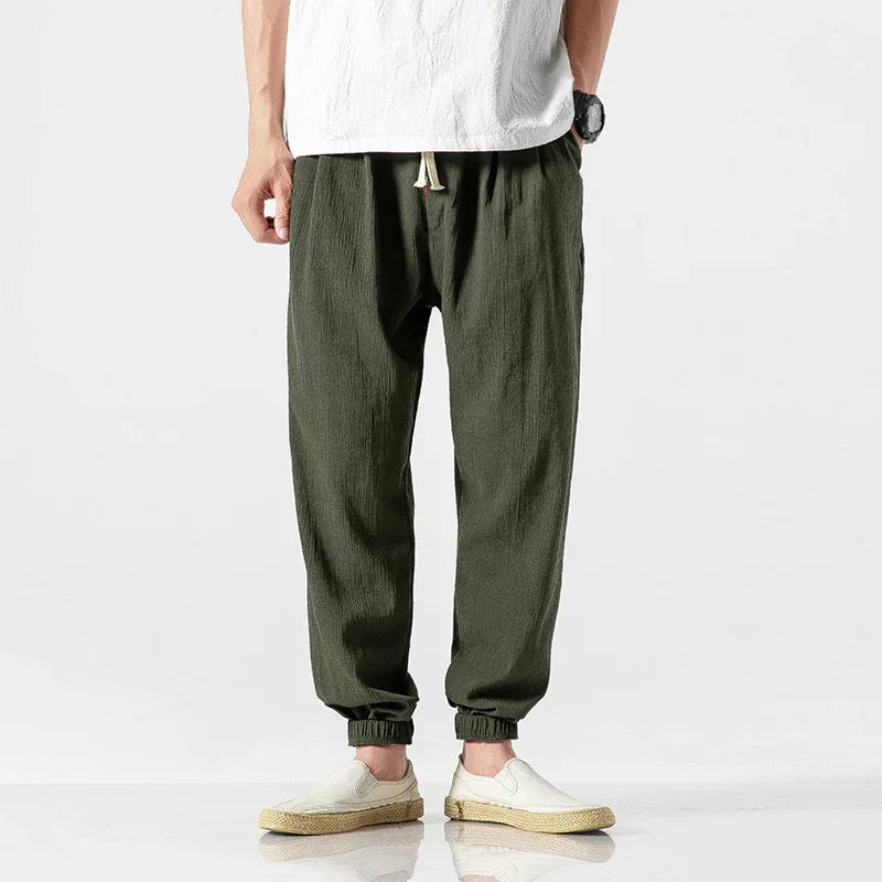 Man wearing casual olive green jogger pants with elastic cuffs and white slip-on shoes